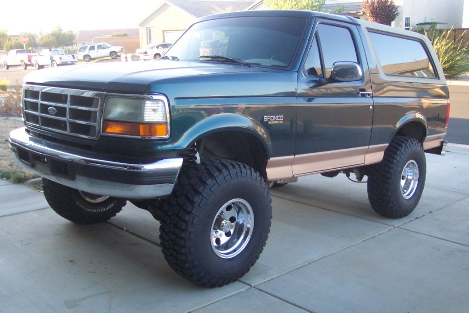 Green 1995 Ford Bronco with tan trim and large off-road tires, parked on a concrete driveway