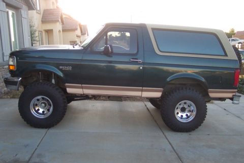 1995 Ford Bronco - This lifted 1995 Ford Bronco is parked on a paved surface in front of a house.