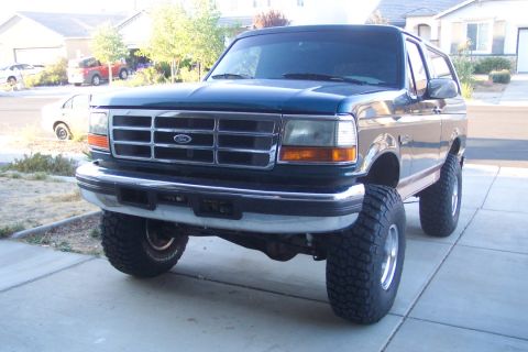 1995 Ford Bronco - A lifted dark blue Ford Bronco is parked in a driveway, showing off its large tires and modified suspension.