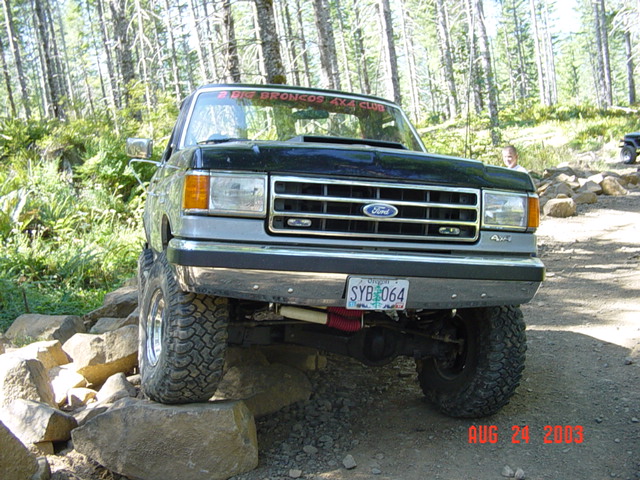 Front view of lifted Ford Bronco flexing over rocks, Lower Mainland 4x4 Club banner