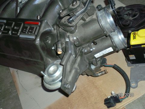 1996 Ford Bronco - Ford 5.8L EFI upper intake manifold laid on cardboard with the throttle body, throttle linkage bracket and EGR spacer bolted in place, plus…