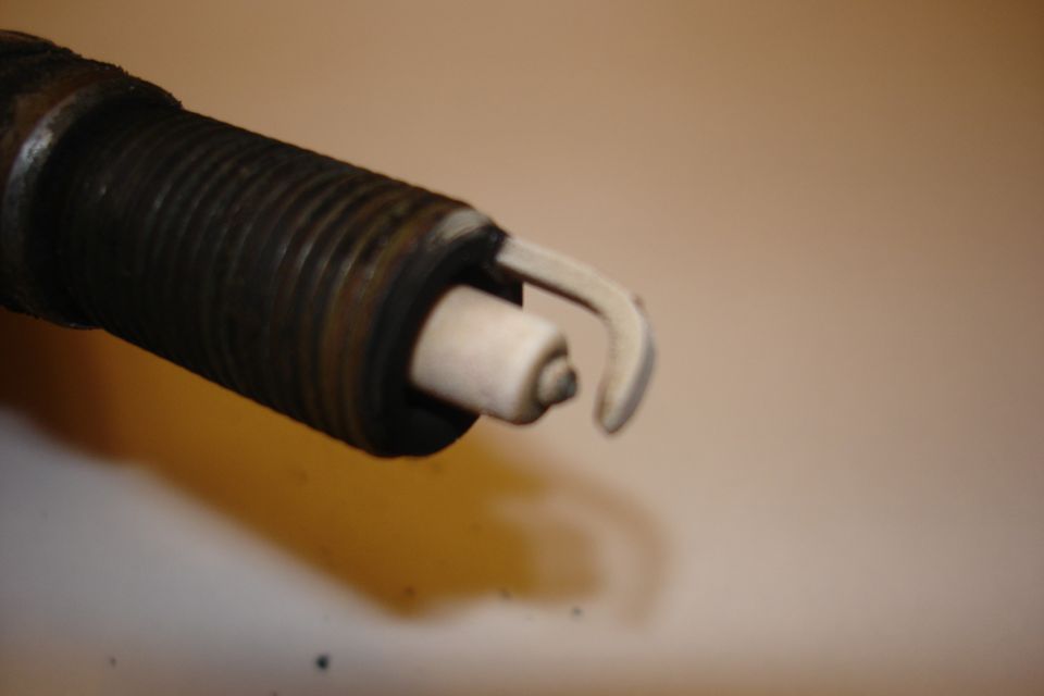 Close-up of a used spark plug firing end with white deposits on the ground strap