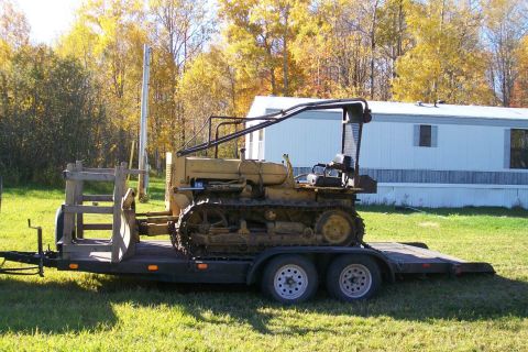 2000 Chevrolet Tahoe - A yellow crawler tractor is loaded onto a dual-axle trailer, parked on a grassy area with trees and a mobile home in the background.
