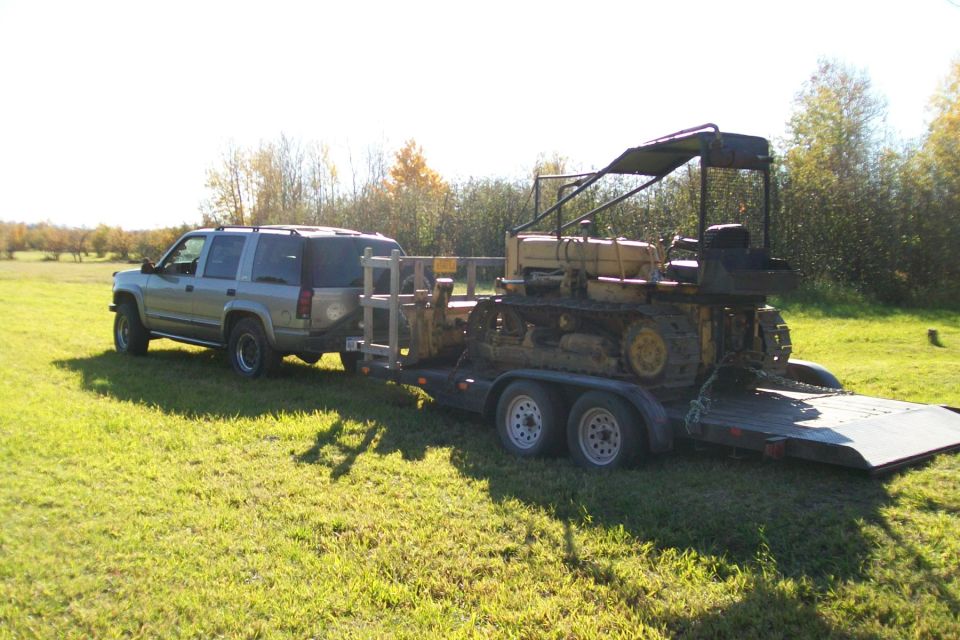 Silver SUV towing a yellow bulldozer on a trailer in a grassy field
