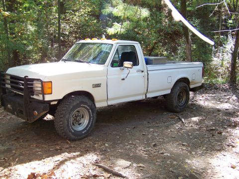 1987 Ford F-250 - This white 1987 Ford F-250 pickup truck is parked on a dirt path surrounded by trees.