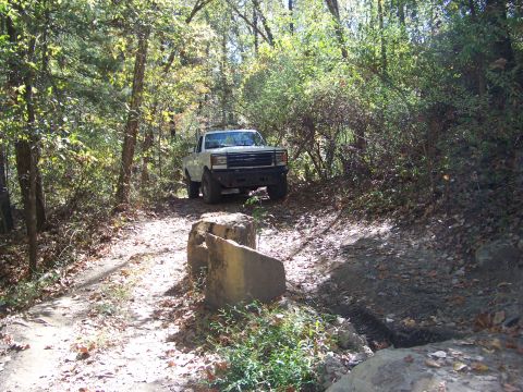 1987 Ford F-250 - A white pickup truck navigates a wooded trail with rough terrain.