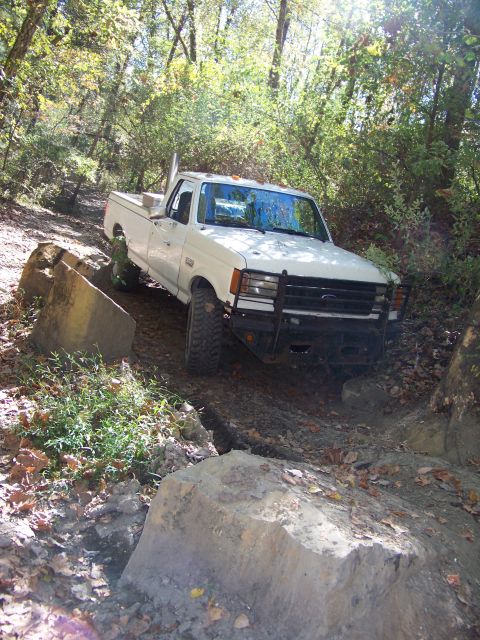1987 Ford F-250 - A white 1987 Ford F-250 pickup truck navigates a rocky, wooded trail.