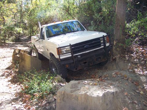 1987 Ford F-250 - This 1987 Ford F-250 navigates a challenging off-road course with large rocks and trees.