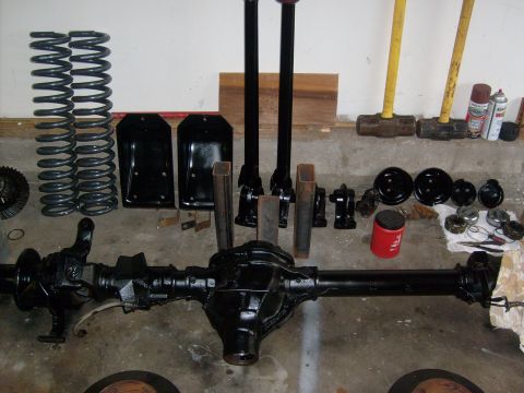 1986 Ford Bronco - Various automotive parts, including an axle, springs, and shocks, are arranged on a garage floor.