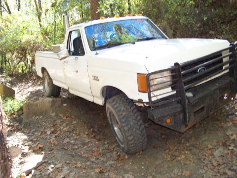 1987 Ford F-250 - A white 1987 Ford F-250 pickup truck is shown from a 3/4 front angle, parked on an uneven, wooded terrain.