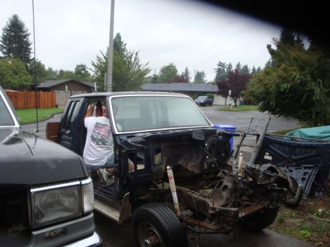 1989 Ford Bronco - A dark blue Ford truck being stripped for a rebuild sits in a suburban driveway, its cab and bed pulled apart and front sheet metal removed…