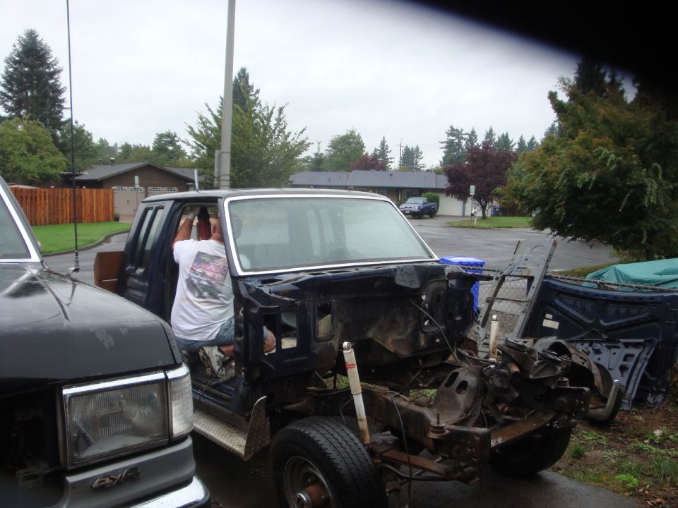 Dark blue Ford truck stripped for rebuild in a driveway, man working in cab