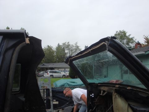 1989 Ford Bronco - A man works on the interior of a disassembled vehicle, possibly a Ford Bronco, under an overcast sky.