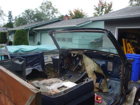 1989 Ford Bronco - Gutted dark blue Ford truck cab shell in a residential driveway, stripped down to bare floor pan, firewall and rear glass with all seats, t…