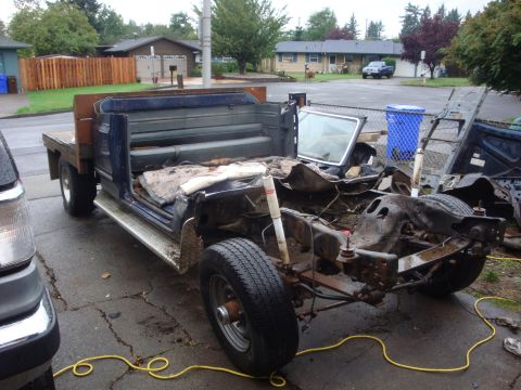1989 Ford Bronco - A dark blue flatbed pickup sits stripped in a residential driveway with its cab front, doors, fenders, hood and engine removed, exposing th…