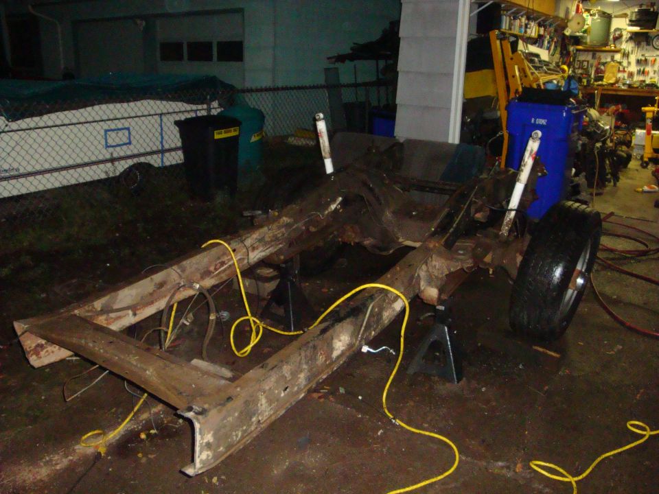 Bare rusty truck frame on jack stands outside a garage during a chassis teardown