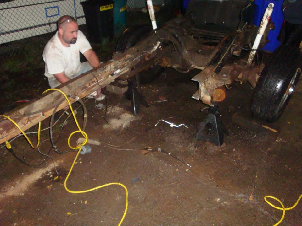 Person working on a bare rusty truck frame on jack stands with body removed