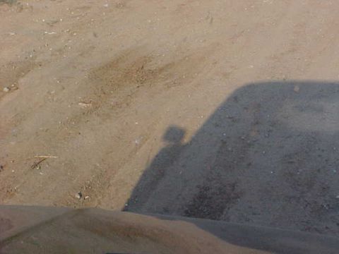 1989 Ford Bronco - A shadow of a person and a vehicle is cast on a dirt road.
