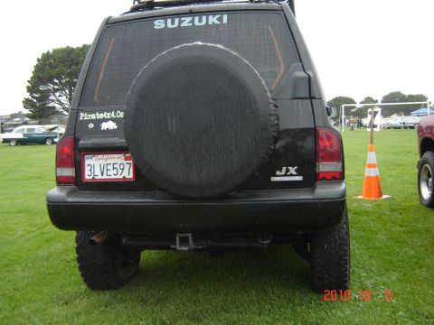 1993 Ford Bronco - Rear view of a black Suzuki Vitara parked on grass, with other vehicles and a field in the background.