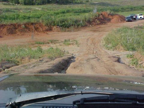 1989 Ford Bronco - View from inside a vehicle shows a dirt road with several parked cars in the distance.