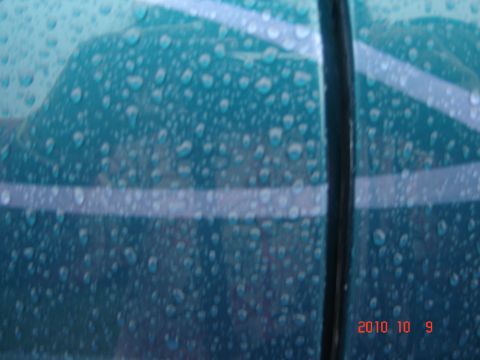 1993 Ford Bronco - Water droplets cover the side of a teal vehicle, obscuring details of its make and model.