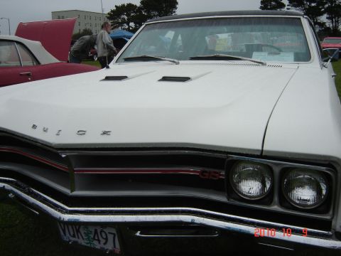1993 Ford Bronco - Front view of a white 1967 Buick GS, its distinctive chrome grille and dual headlights. Another vehicle is partially visible to the left.