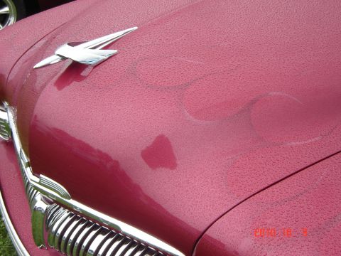 1993 Ford Bronco - Water droplets cover the hood and grille of a classic red car, highlighting its chrome details.