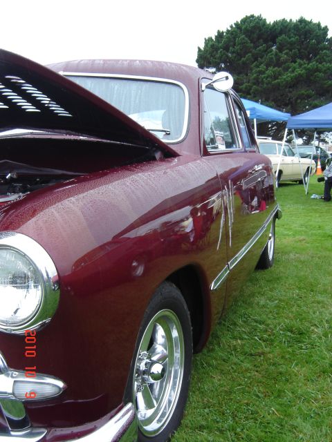 1993 Ford Bronco - A maroon sedan with its hood open is displayed on a grassy field next to other vehicles.