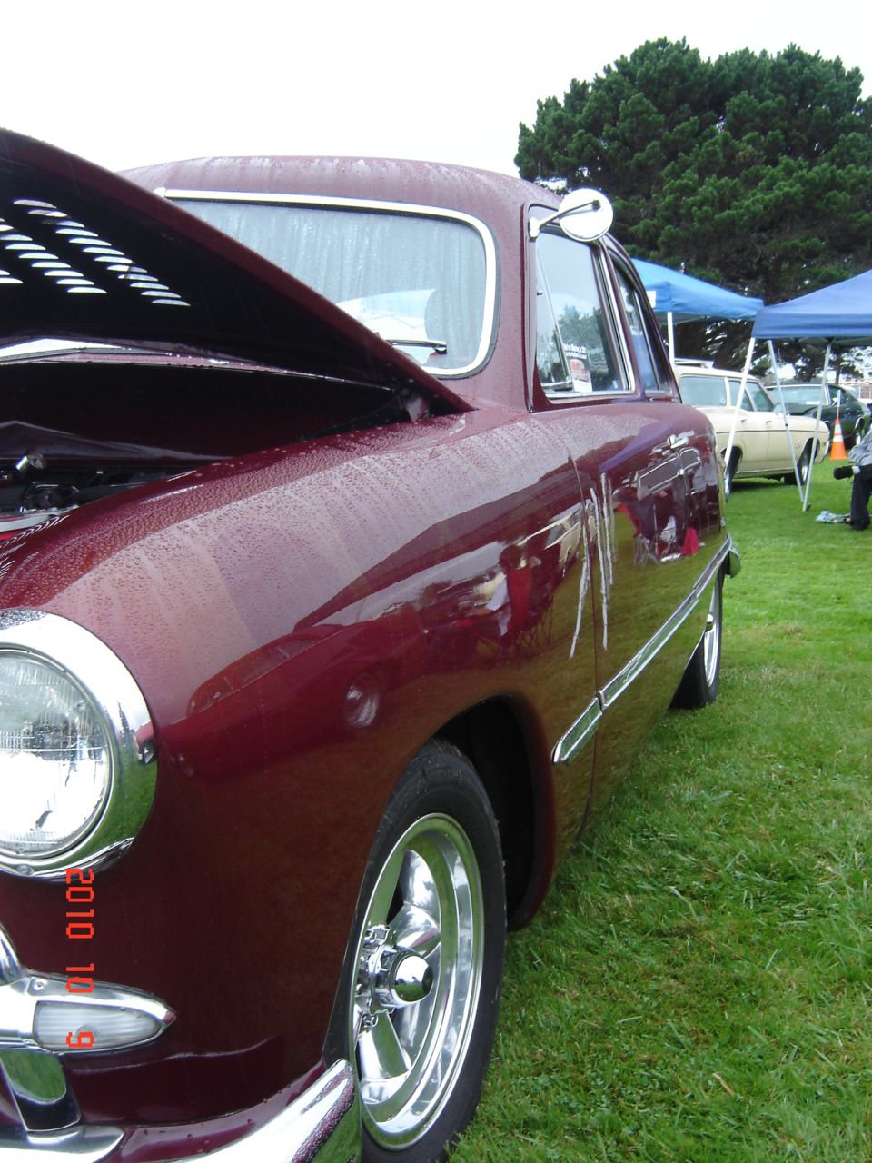 Maroon sedan with hood open, chrome trim, and aftermarket wheels parked on grass