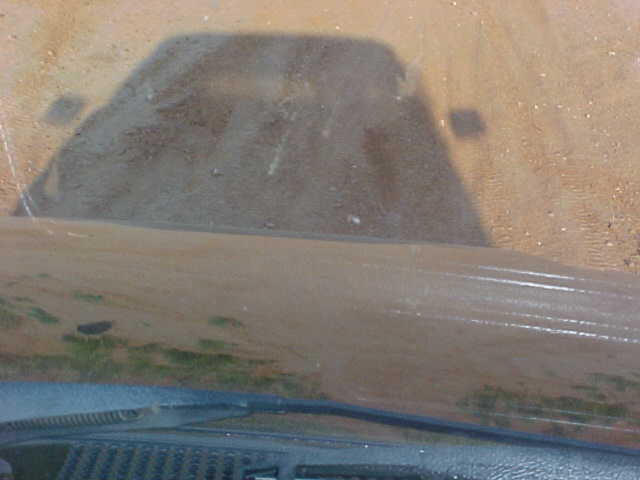 Shadow of a vehicle on a dusty ground, seen through a dirty windshield