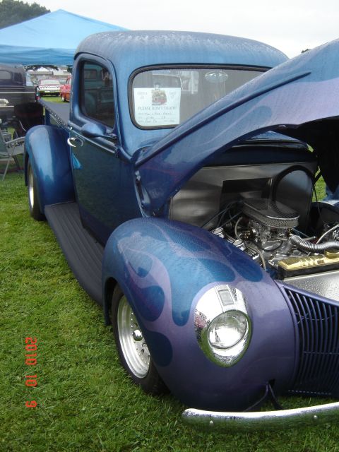 1993 Ford Bronco - A custom blue pickup truck with flame graphics is displayed with its hood open, revealing the engine.