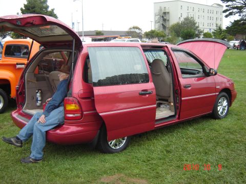 1993 Ford Bronco - Red minivan with all doors open, parked on grass next to an orange truck.