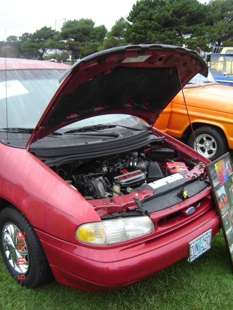 1993 Ford Bronco - The engine bay of a red van is displayed, with an orange truck visible to the right.
