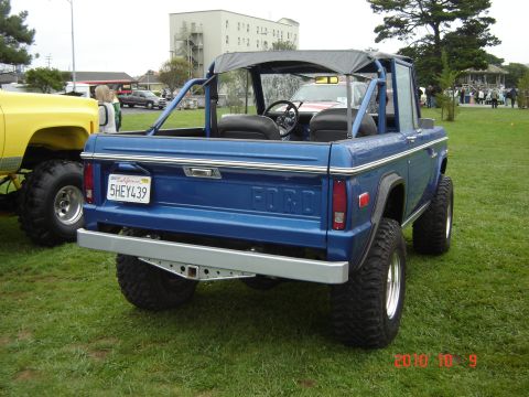 1993 Ford Bronco - A blue Ford Bronco with a soft top is parked on grass next to a yellow truck.