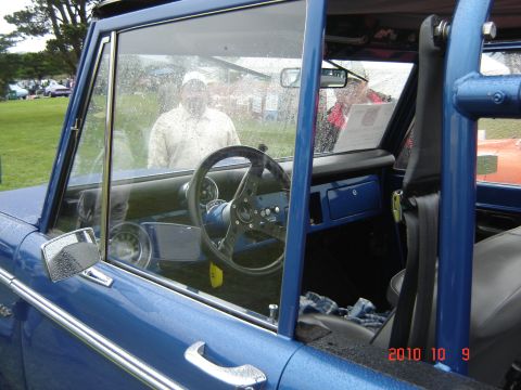 1993 Ford Bronco - The interior of a blue Ford Bronco shows a roll cage and aftermarket steering wheel, with two people visible outside.