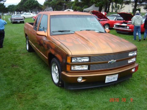 1993 Ford Bronco - A customized Chevrolet pickup truck with flame graphics is parked on grass at an outdoor event.
