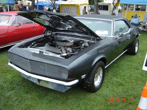 1993 Ford Bronco - A dark gray coupe is displayed with its hood open, revealing the engine bay, while a red car is parked alongside it on a grassy area.