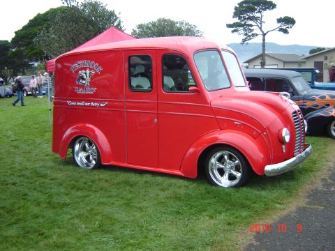 1993 Ford Bronco - A vintage red panel van with custom wheels is parked on a grassy field next to other vehicles.