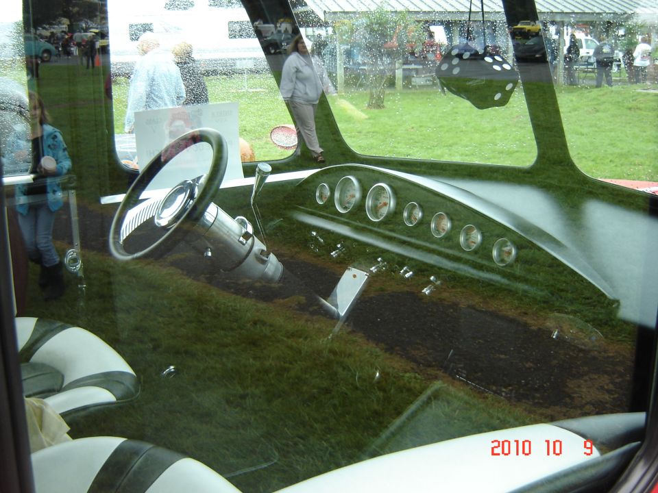 Custom hot rod interior with green carpet, white and dark green seats, and a chrome steering wheel