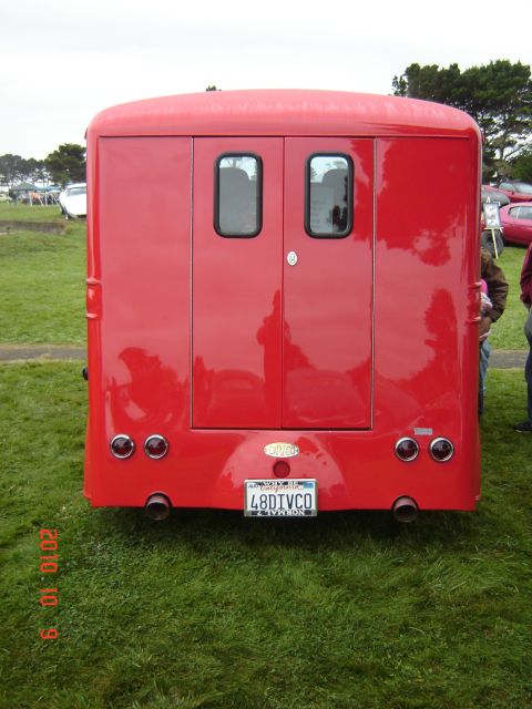 1993 Ford Bronco - This red van features a distinctive rear design with double doors and dual exhaust pipes, seen at an outdoor event.