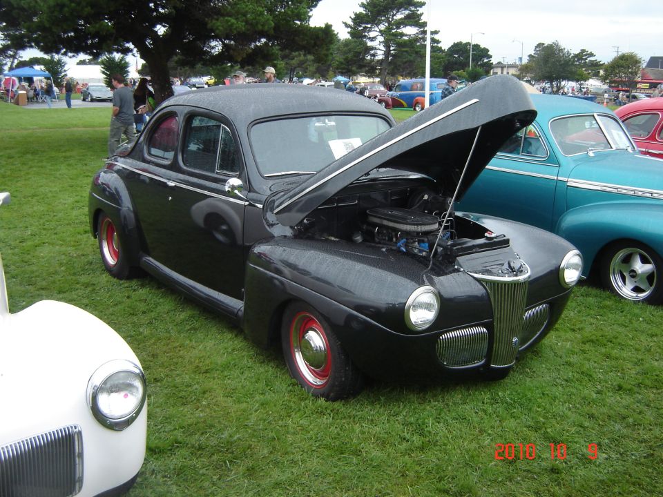 Black 1941 coupe with hood open, red wheels, parked on grass
