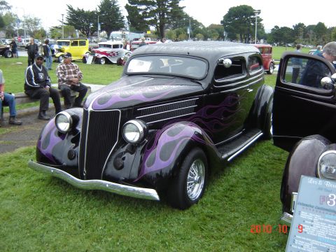 1993 Ford Bronco - A customized black sedan with purple flame graphics is displayed at an outdoor car show.