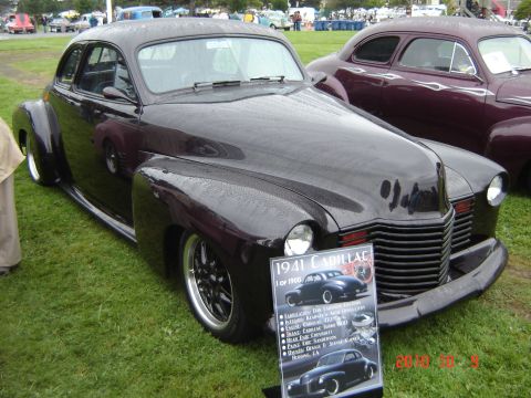 1993 Ford Bronco - A dark purple 1941 Cadillac coupe is displayed on a grassy field, with a sign detailing its specifications.