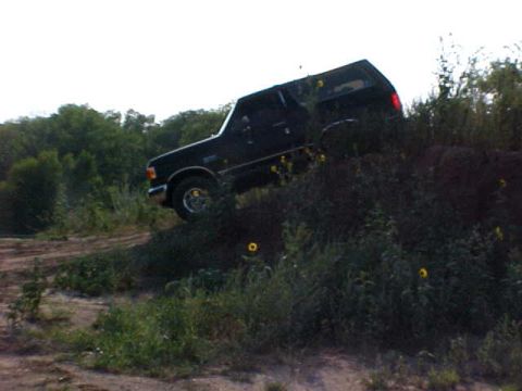 1989 Ford Bronco - A black Ford Bronco navigates a steep, grassy incline with trees in the background.