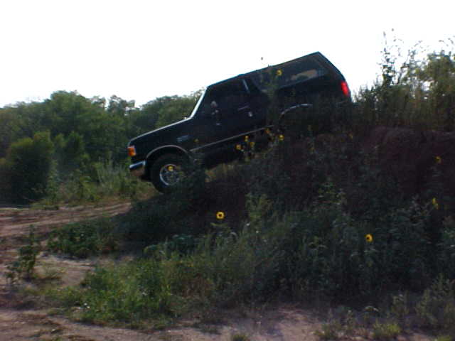 Black Ford Bronco climbing a dirt hill, side view