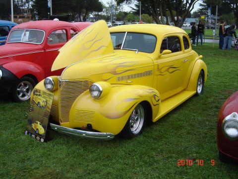 1993 Ford Bronco - A custom yellow hot rod with flame decals is displayed at an outdoor event, with other vehicles nearby.