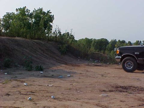 1989 Ford Bronco - A black 1989 Ford Bronco is seen from the front-right in a dusty, outdoor setting with trees and debris scattered around.