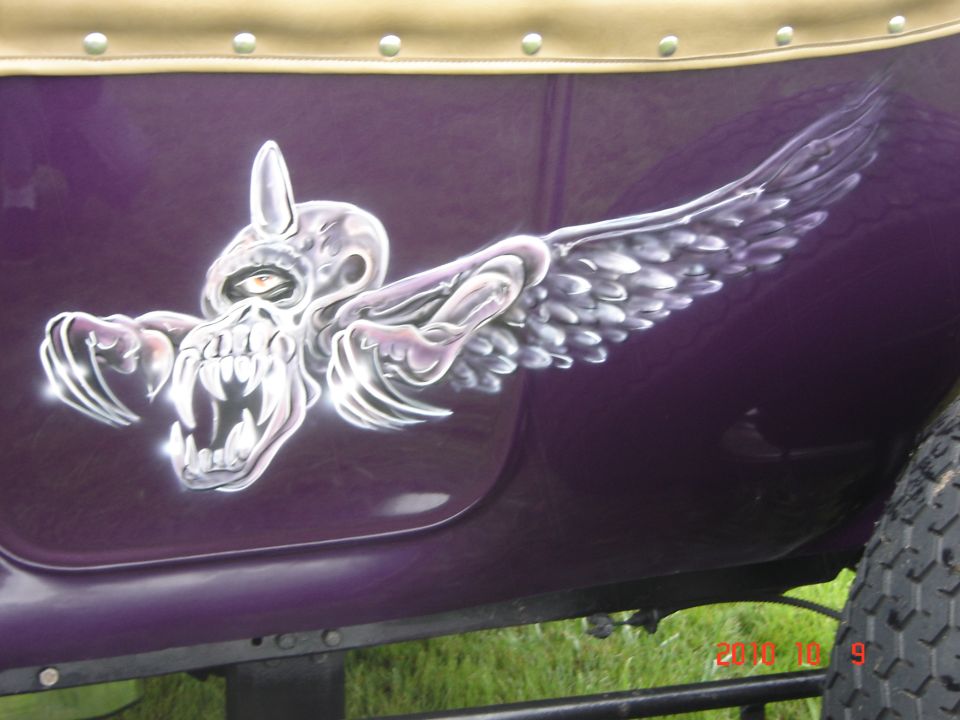 Purple vehicle side with airbrushed skull and wings graphic. Part of a tire is visible