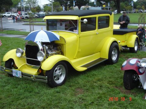 1993 Ford Bronco - A bright yellow hot rod with a black roof and a trailer is parked on grass, with an umbrella covering its exposed engine.