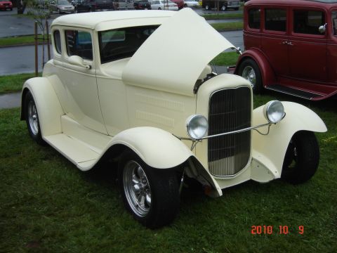 1993 Ford Bronco - A cream-colored hot rod coupe is parked on grass, with its hood open, next to a red sedan.